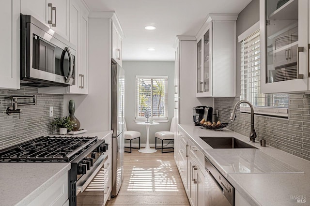 kitchen with a sink, white cabinetry, glass insert cabinets, and appliances with stainless steel finishes