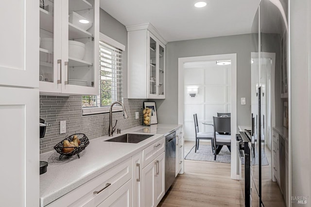 kitchen with a sink, light wood finished floors, appliances with stainless steel finishes, white cabinets, and decorative backsplash