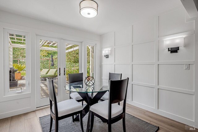 dining room with a decorative wall, a healthy amount of sunlight, french doors, and light wood finished floors