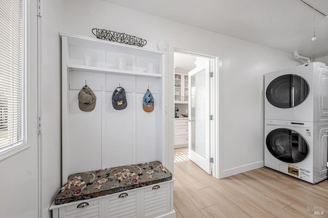 clothes washing area featuring laundry area, baseboards, stacked washing maching and dryer, and light wood-style floors