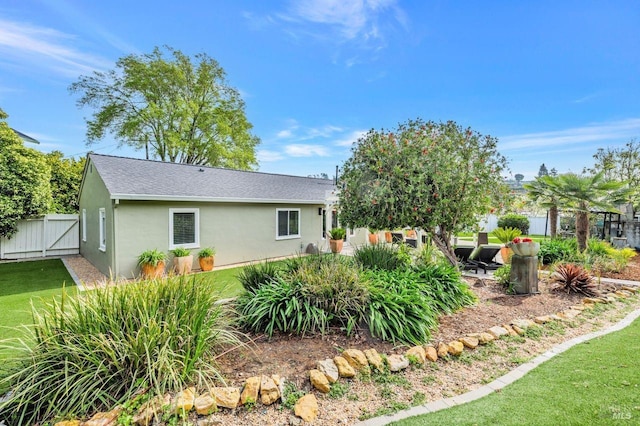 exterior space with a lawn, stucco siding, fence, and roof with shingles