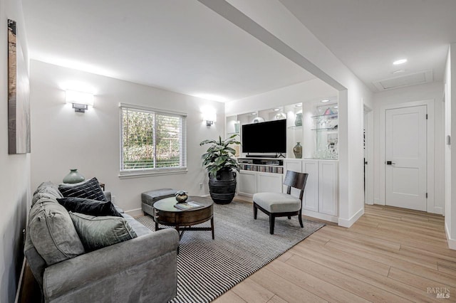 living area featuring baseboards, light wood-type flooring, and attic access