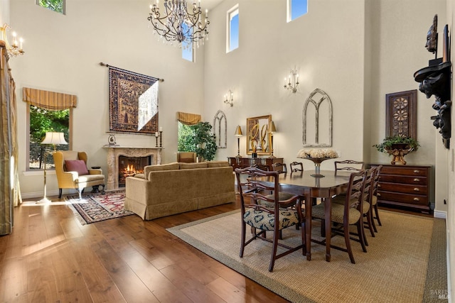 dining area with a chandelier, hardwood / wood-style floors, a high ceiling, and a lit fireplace