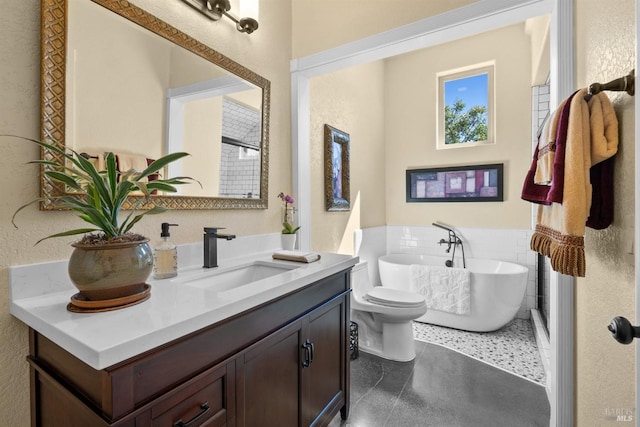 full bath with a textured wall, a freestanding tub, toilet, and vanity