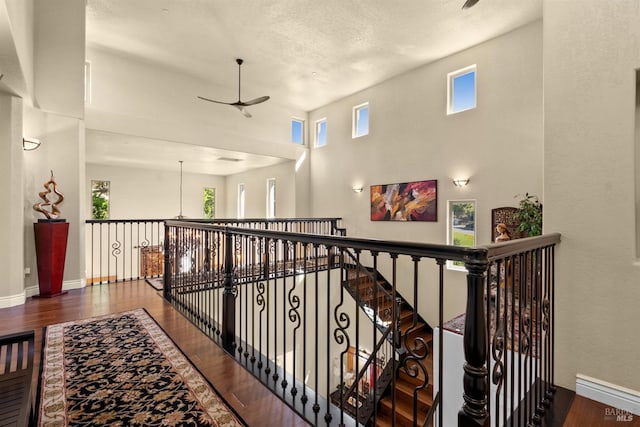 corridor featuring an upstairs landing, baseboards, a towering ceiling, and wood finished floors