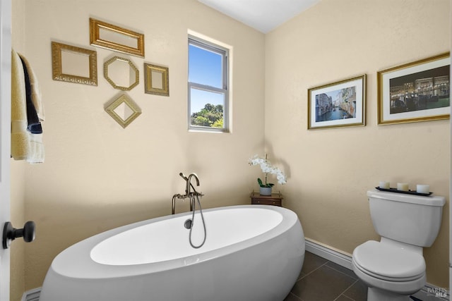 bathroom featuring a freestanding tub, toilet, baseboards, and tile patterned floors