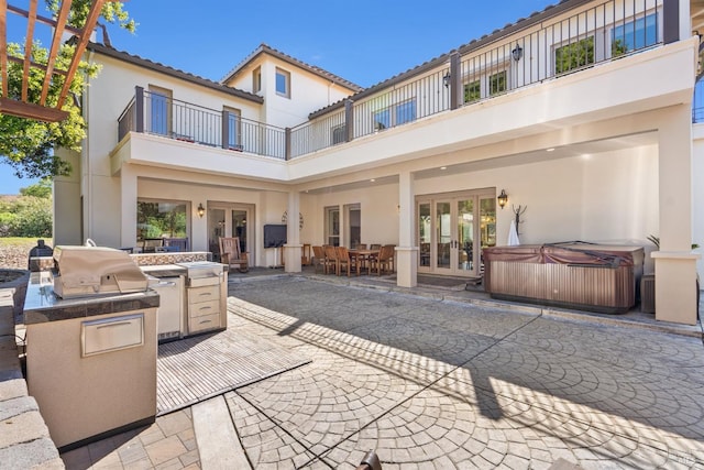 back of house with exterior kitchen, a balcony, a patio area, french doors, and a hot tub
