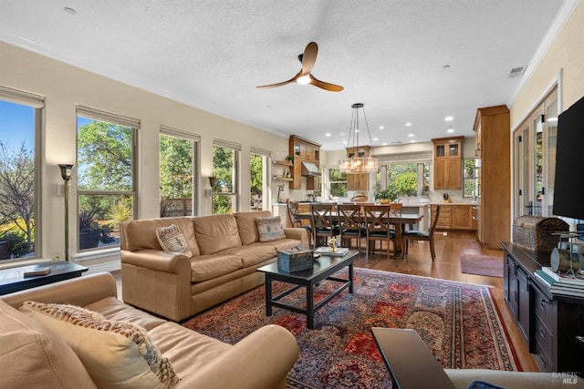 living area with ceiling fan with notable chandelier, recessed lighting, crown molding, and dark wood-style flooring