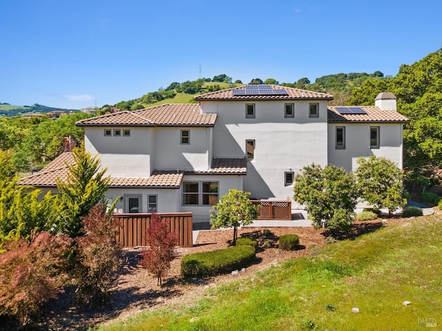 back of house featuring a chimney, a tiled roof, roof mounted solar panels, a yard, and stucco siding