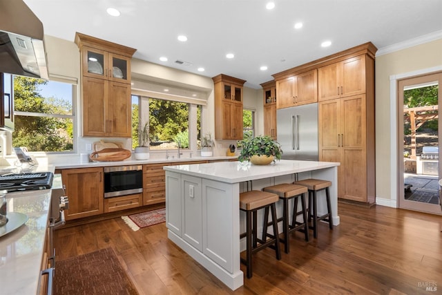 kitchen featuring recessed lighting, under cabinet range hood, a center island, a kitchen bar, and built in appliances