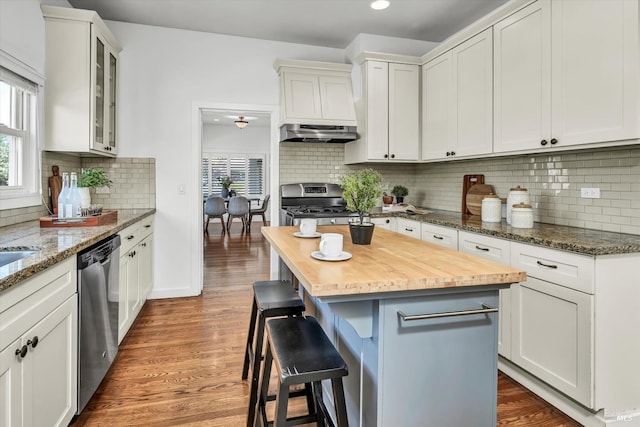 kitchen with a kitchen bar, under cabinet range hood, wood finished floors, stainless steel appliances, and wood counters