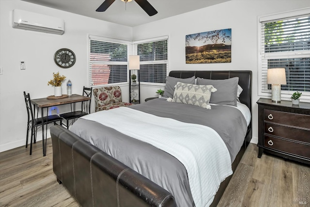 bedroom featuring an AC wall unit, baseboards, light wood finished floors, and a ceiling fan