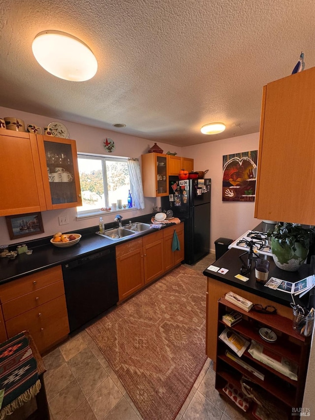 kitchen with dark countertops, glass insert cabinets, a sink, black appliances, and brown cabinetry