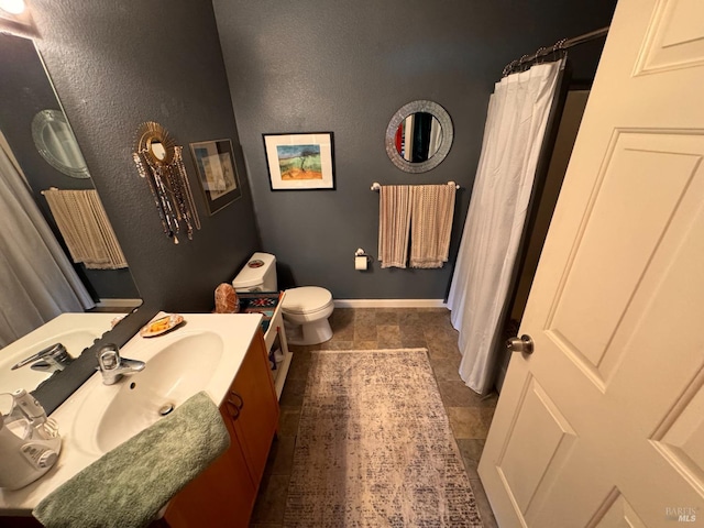 full bath featuring vanity, toilet, a textured wall, a shower with shower curtain, and baseboards