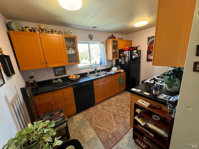 kitchen featuring a textured ceiling, glass insert cabinets, a sink, black appliances, and brown cabinetry
