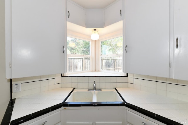 kitchen featuring tile counters, white cabinets, and a sink