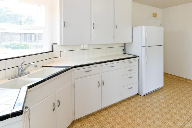 kitchen featuring backsplash, freestanding refrigerator, tile counters, white cabinetry, and light floors