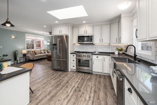 kitchen with light wood-style flooring, backsplash, dark countertops, high end appliances, and a sink