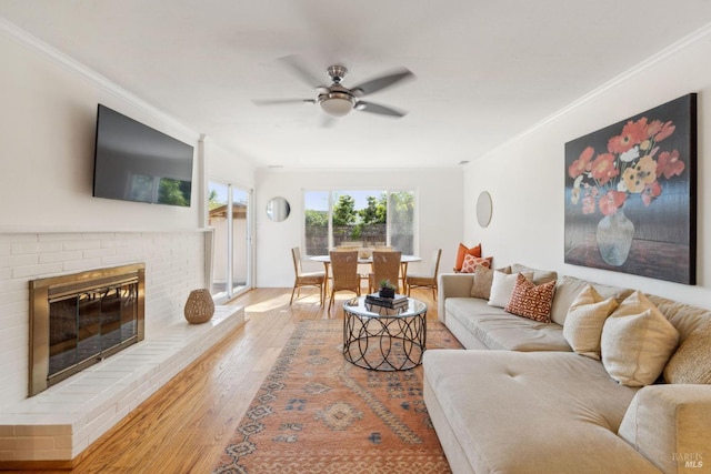 living room with crown molding, a ceiling fan, a brick fireplace, and wood finished floors