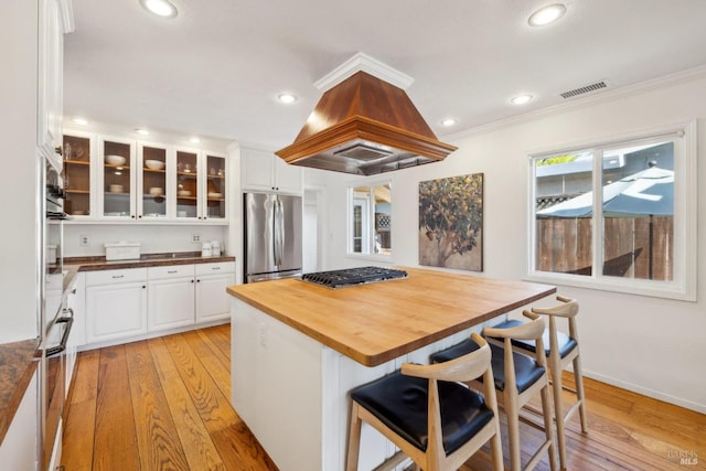 kitchen with stainless steel appliances, white cabinetry, light wood-type flooring, visible vents, and butcher block counters