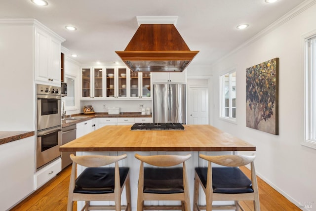 kitchen featuring a kitchen breakfast bar, appliances with stainless steel finishes, butcher block counters, custom range hood, and white cabinetry
