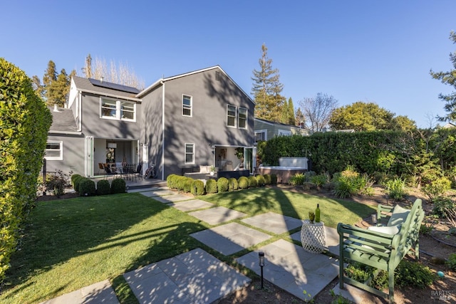 rear view of property with roof mounted solar panels, stucco siding, a patio, and a yard
