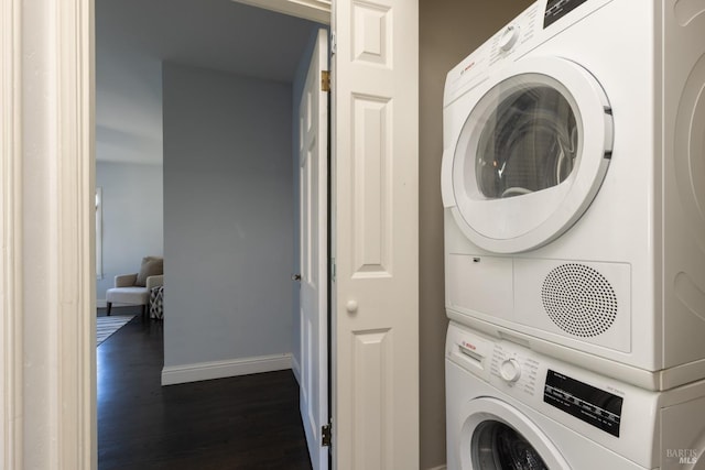 washroom featuring baseboards, dark wood-style flooring, stacked washer / dryer, and laundry area
