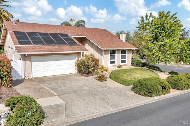 view of front of home featuring a garage, solar panels, a chimney, a shingled roof, and driveway