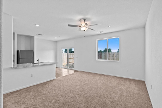 unfurnished living room featuring visible vents, a sink, carpet, and ceiling fan