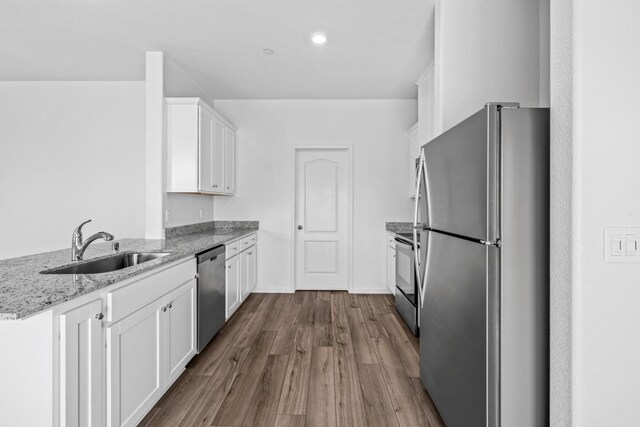 kitchen with light stone countertops, a sink, stainless steel appliances, white cabinetry, and wood finished floors