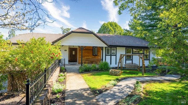 view of front facade with a tile roof, a front yard, covered porch, and stucco siding