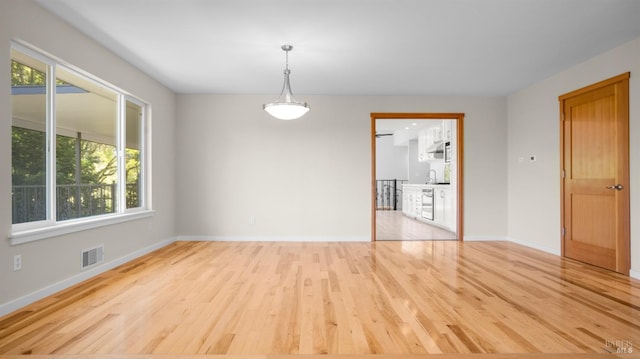 empty room with wood finished floors, a sink, baseboards, and visible vents