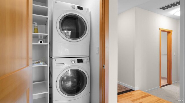 laundry room featuring visible vents, stacked washer / dryer, baseboards, wood finished floors, and laundry area