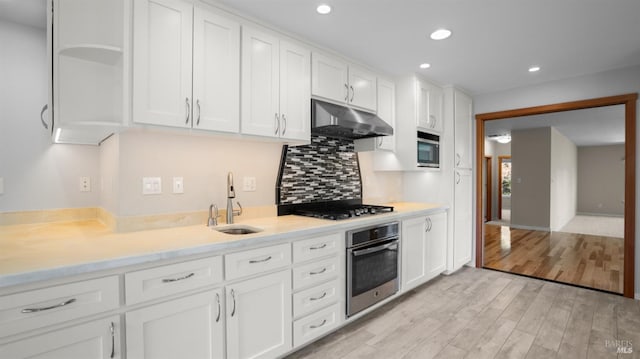 kitchen with a sink, light wood-style flooring, under cabinet range hood, stainless steel appliances, and white cabinets