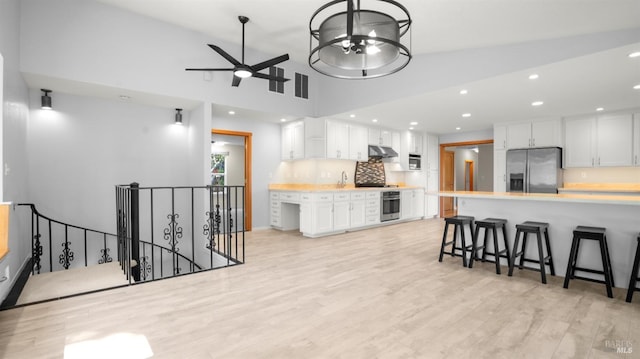 kitchen featuring light countertops, light wood finished floors, stainless steel appliances, white cabinetry, and vaulted ceiling