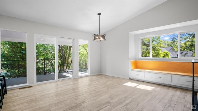 unfurnished dining area with light wood-type flooring, an inviting chandelier, vaulted ceiling, and a wealth of natural light