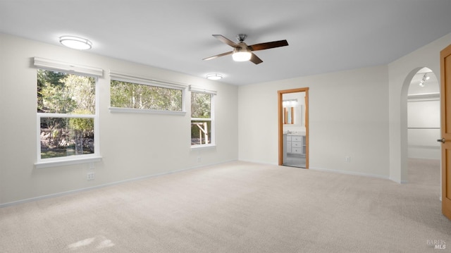 carpeted spare room with baseboards, arched walkways, and ceiling fan
