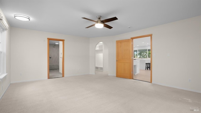 unfurnished room with arched walkways, baseboards, a ceiling fan, and light carpet
