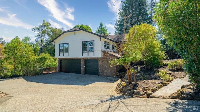 view of front facade featuring driveway, stone siding, fence, a tiled roof, and a garage