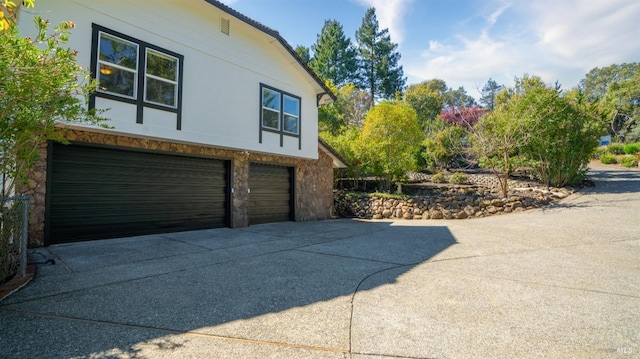 view of property exterior with driveway, stucco siding, stone siding, and a garage