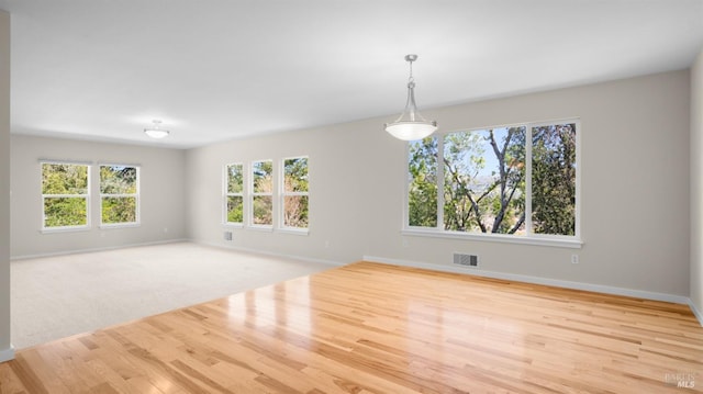 empty room with baseboards, visible vents, a healthy amount of sunlight, and wood finished floors