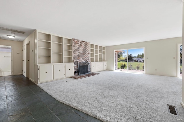 unfurnished living room featuring built in features, stone finish floor, visible vents, a brick fireplace, and baseboards