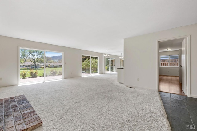 unfurnished living room with visible vents, carpet, a chandelier, and baseboards