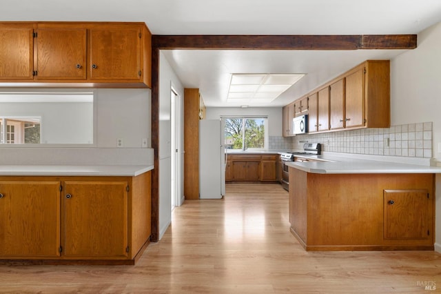 kitchen with light wood-type flooring, a peninsula, light countertops, brown cabinetry, and appliances with stainless steel finishes