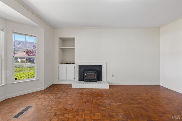 unfurnished living room with crown molding, built in features, a wood stove, visible vents, and baseboards