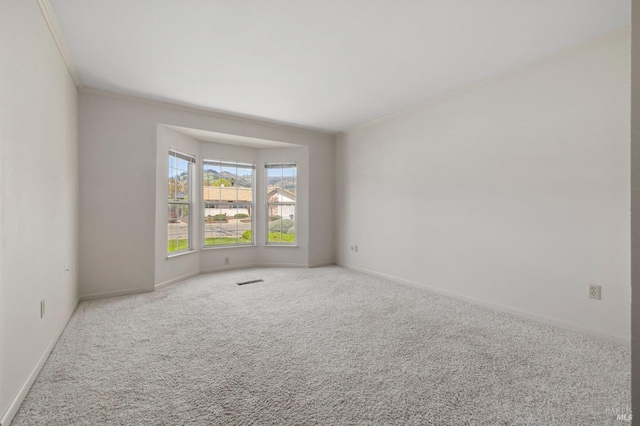 carpeted spare room featuring crown molding, baseboards, and visible vents