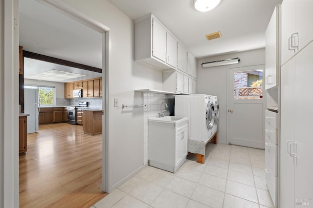 washroom featuring washing machine and dryer, light wood-style flooring, visible vents, cabinet space, and a sink