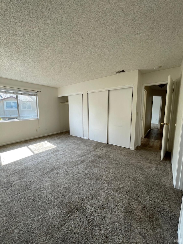 unfurnished bedroom featuring carpet flooring, a textured ceiling, visible vents, and two closets