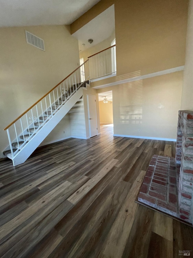 unfurnished living room with high vaulted ceiling, visible vents, baseboards, wood finished floors, and stairway