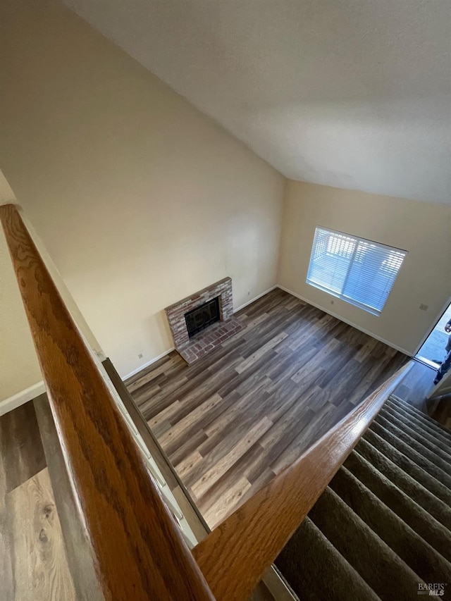 unfurnished living room featuring baseboards, lofted ceiling, a fireplace, and wood finished floors